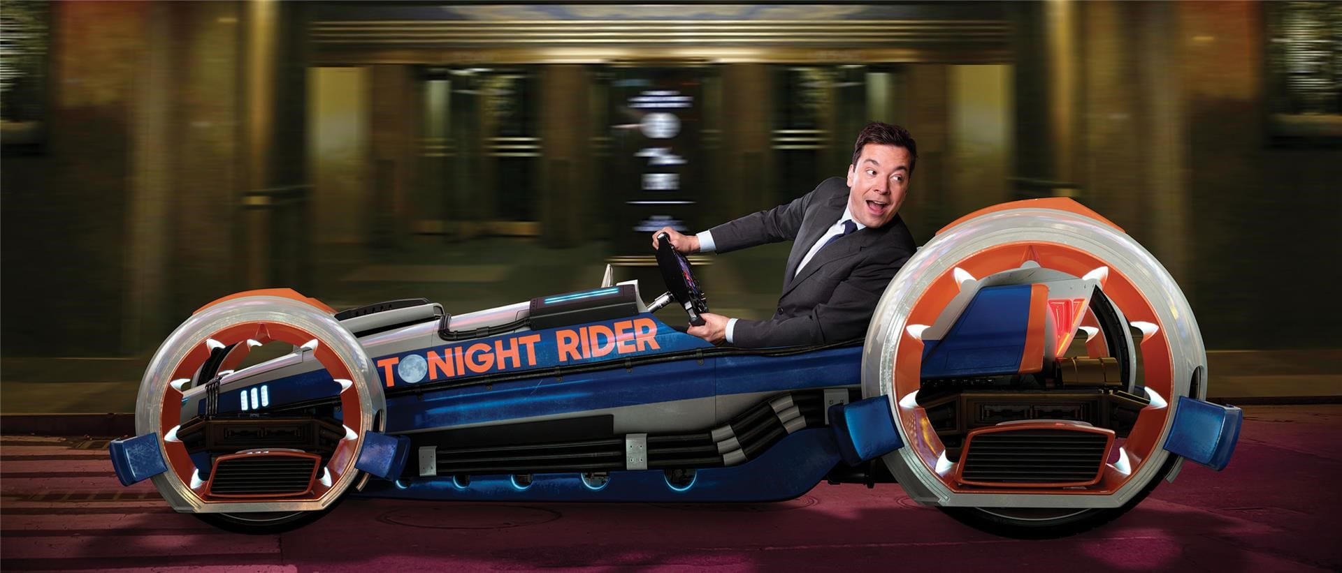 Jimmy Fallon Looks Back Over His Shoulder As He Speeds Along In A Blue And Red