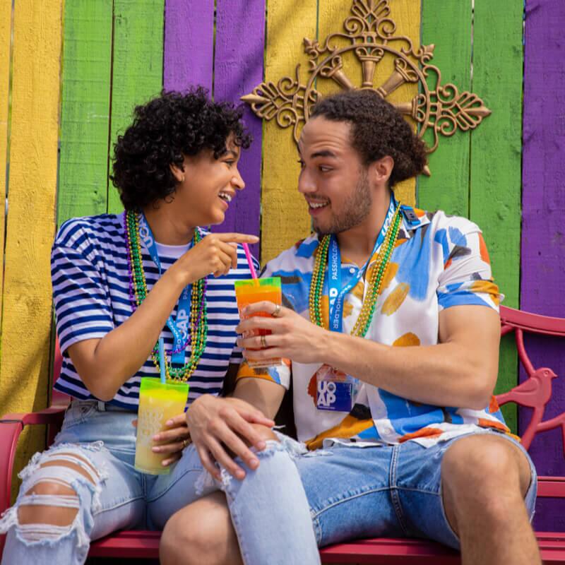 Two Universal Orlando Annual Passholders relax on a bench while enjoying a drink from Universal's Mardi Gras: International Flavors of Carnaval. 