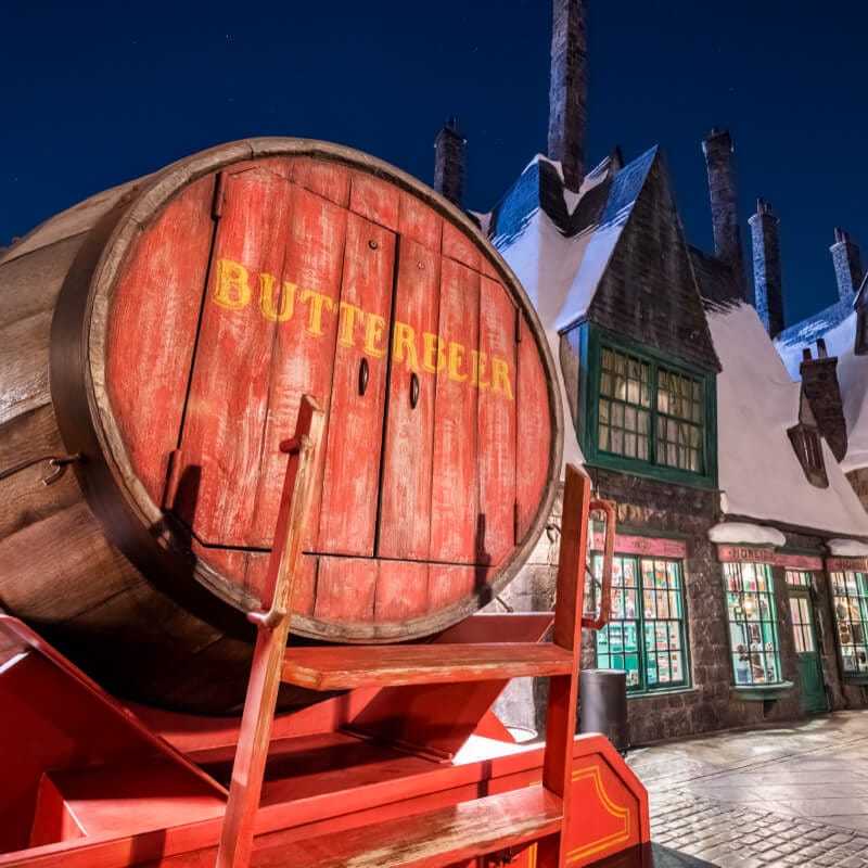 A cart holding a barrel of Butterbeer™ in the streets of snowy Hogsmeade™.