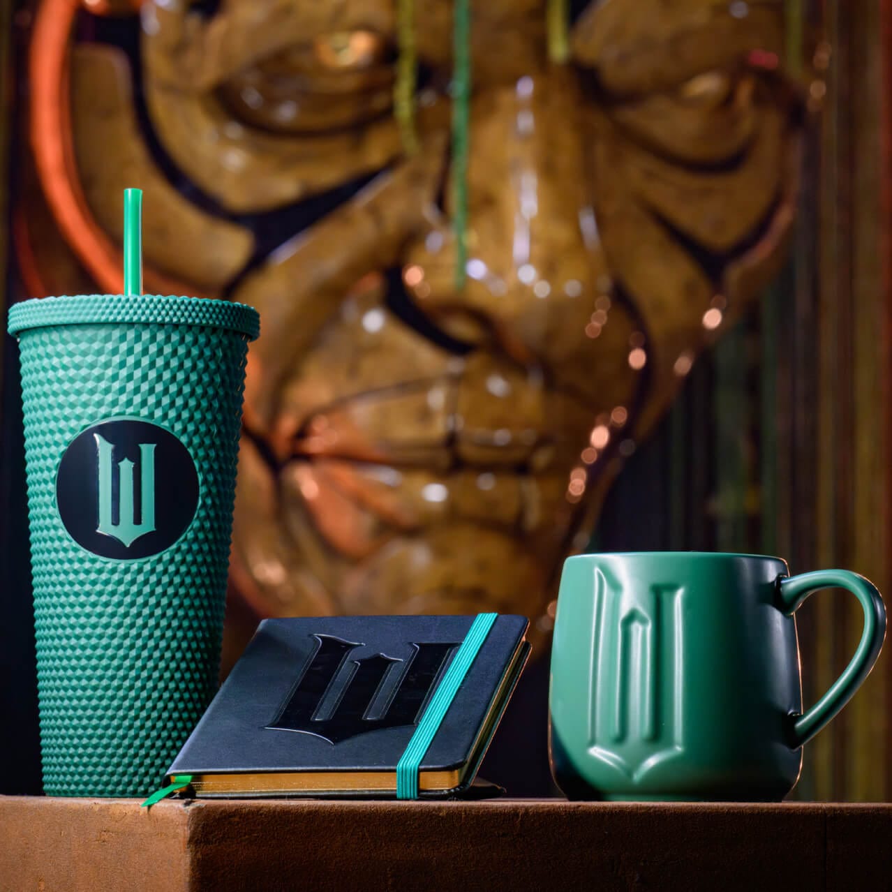 Wicked themed merchandise including a green tumbler, a green coffee mug and a black and green notebook featuring a large W in the center.