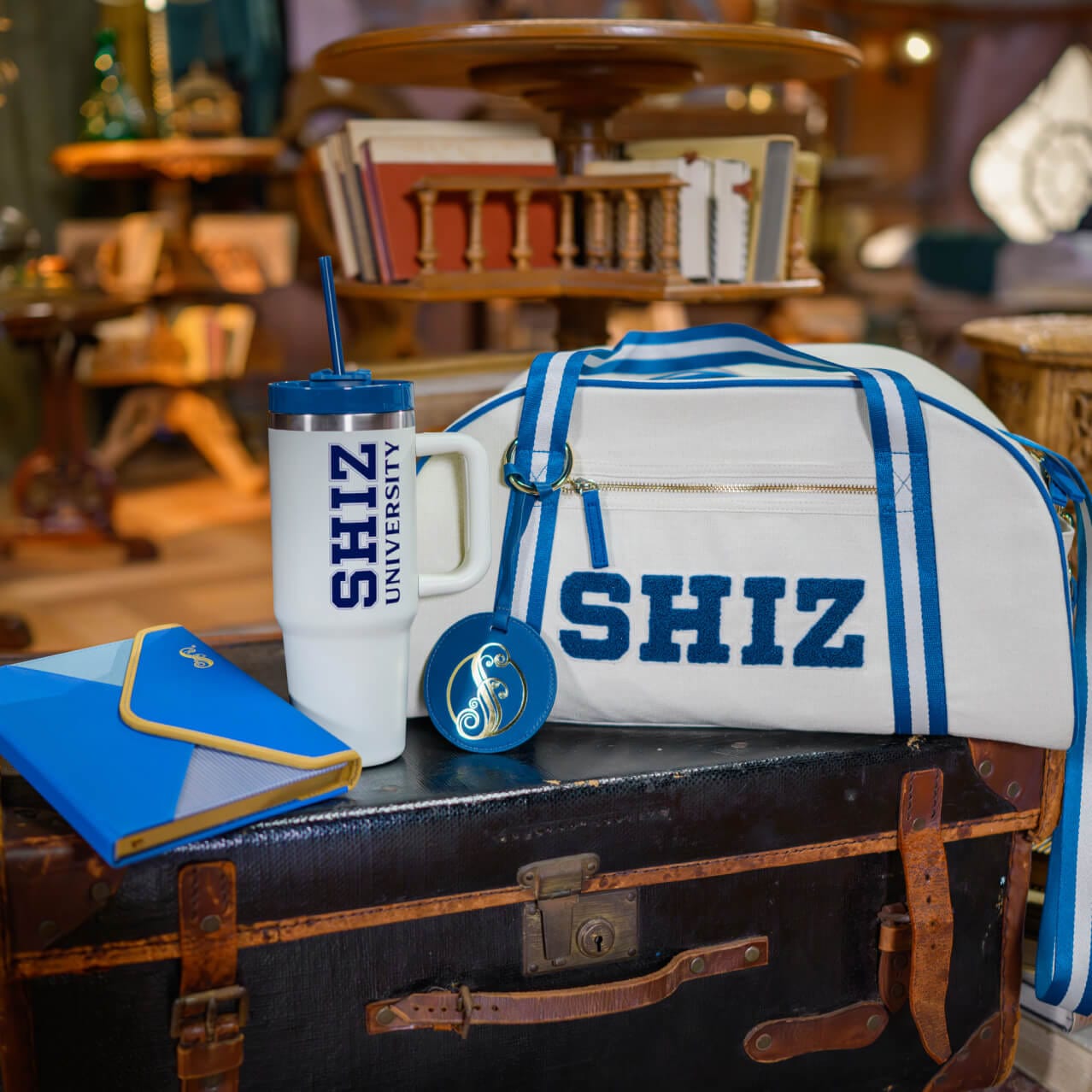 Custom Wicked merchandise including a blue notebook, a tumbler and a duffle bag featuring the word SHIZ.